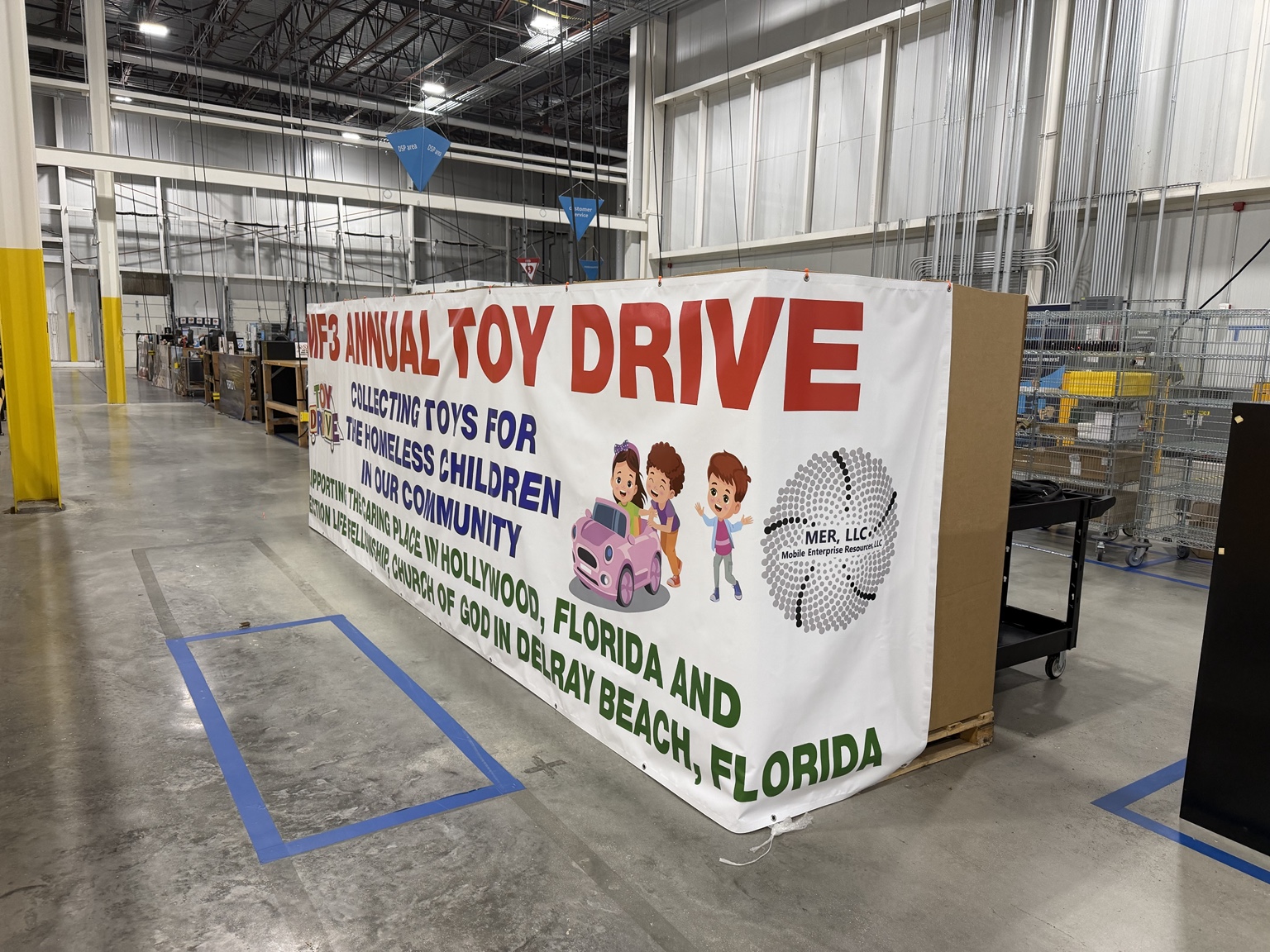 Full side view of the DMF3 Annual Toy Drive banner inside the local Amazon facility